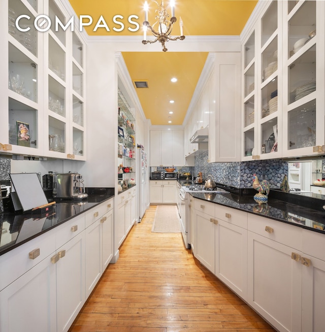 kitchen featuring white appliances, under cabinet range hood, white cabinets, light wood-style floors, and crown molding