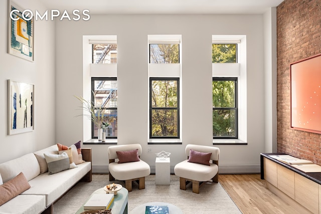 sitting room featuring light wood-style floors, brick wall, and a high ceiling