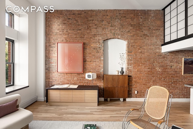 sitting room with a towering ceiling, light wood finished floors, and brick wall