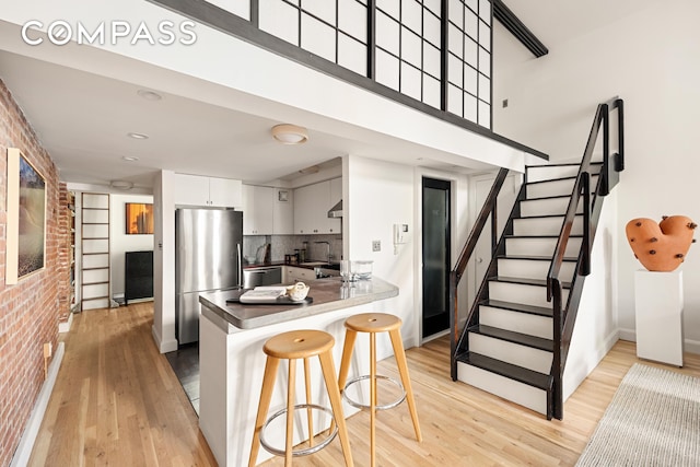 kitchen with light wood finished floors, a kitchen breakfast bar, white cabinetry, and freestanding refrigerator