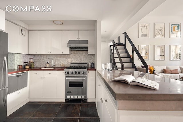 kitchen featuring luxury range, under cabinet range hood, a sink, a peninsula, and decorative backsplash