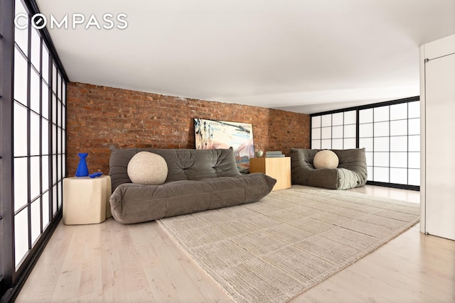 living area featuring a wealth of natural light, wood finished floors, brick wall, and expansive windows