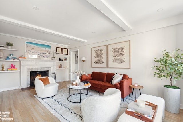 living area with beamed ceiling, a fireplace with flush hearth, and light wood-style flooring