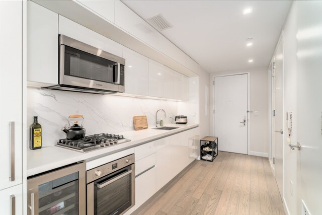 kitchen featuring sink, stainless steel appliances, wine cooler, white cabinets, and light wood-type flooring