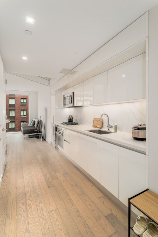 kitchen with sink, white cabinetry, appliances with stainless steel finishes, light hardwood / wood-style floors, and backsplash