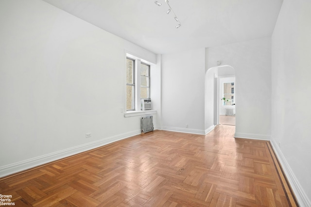 empty room featuring arched walkways, radiator, plenty of natural light, and baseboards