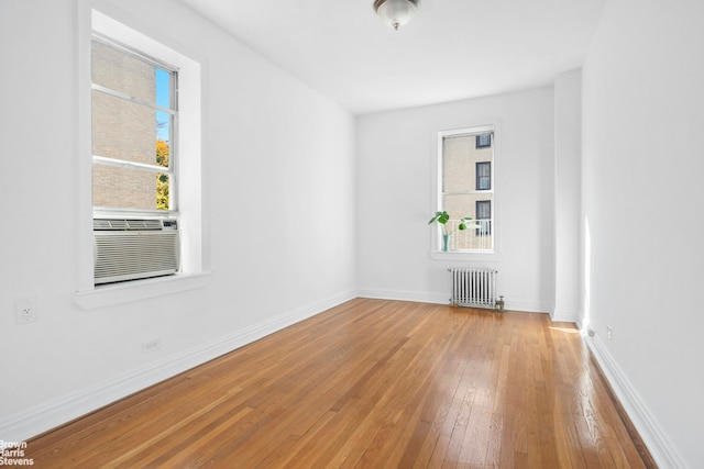 empty room with radiator, wood-type flooring, cooling unit, and plenty of natural light