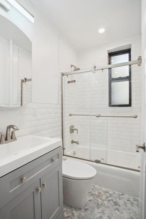 full bathroom with toilet, tile walls, vanity, enclosed tub / shower combo, and decorative backsplash