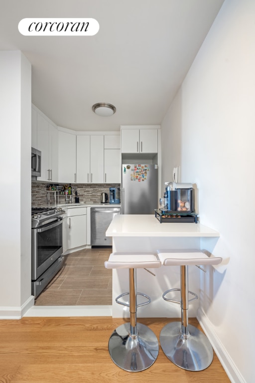 kitchen with appliances with stainless steel finishes, a breakfast bar area, white cabinets, backsplash, and light wood-type flooring