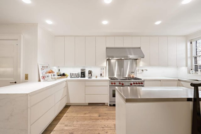 kitchen featuring white cabinetry, high end range, and range hood