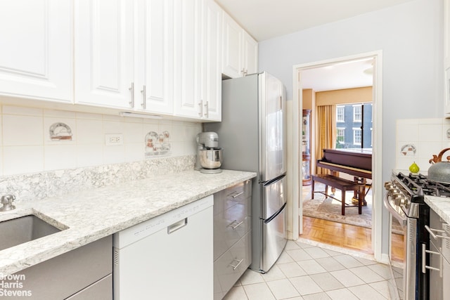 kitchen with appliances with stainless steel finishes, light stone countertops, white cabinetry, and decorative backsplash