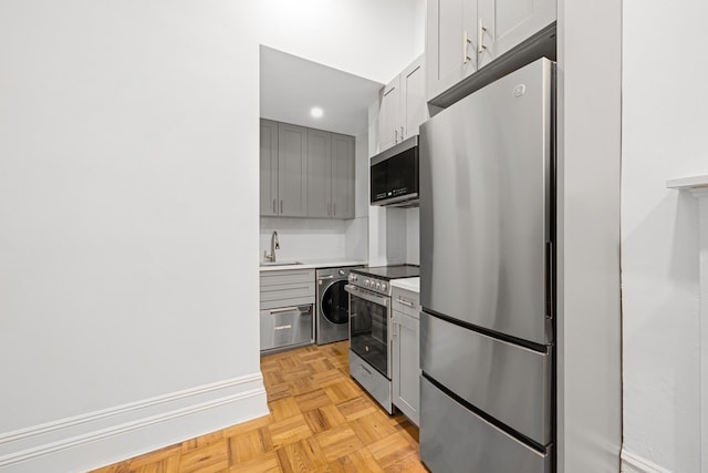 kitchen with stainless steel appliances, washer / clothes dryer, light countertops, gray cabinets, and a sink