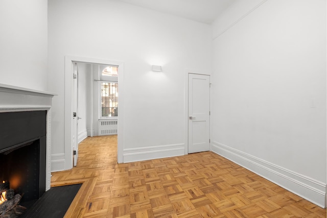 interior space with radiator, a fireplace with flush hearth, a high ceiling, and baseboards