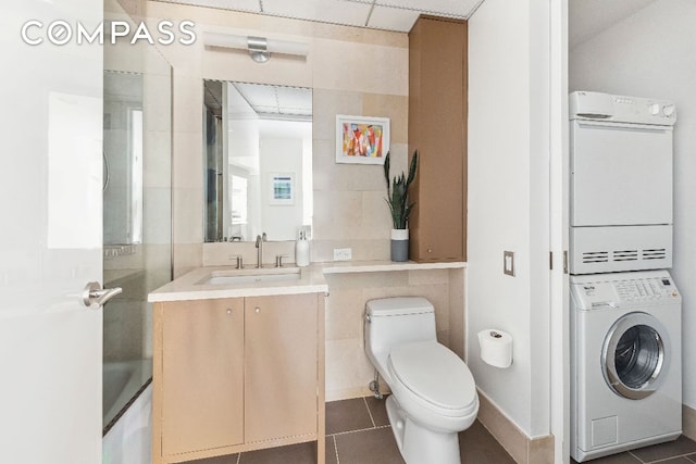 full bathroom with toilet, tile patterned floors, a washtub, vanity, and stacked washing maching and dryer