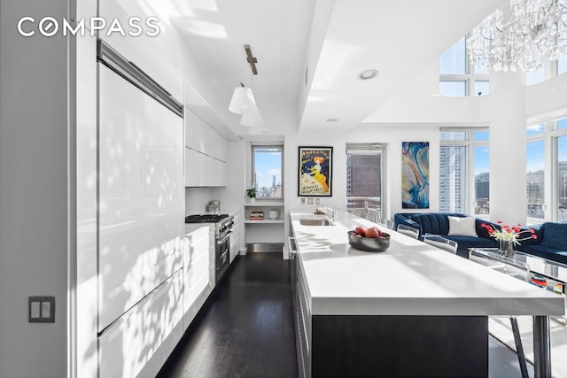 kitchen featuring light countertops, an island with sink, decorative light fixtures, and white cabinetry