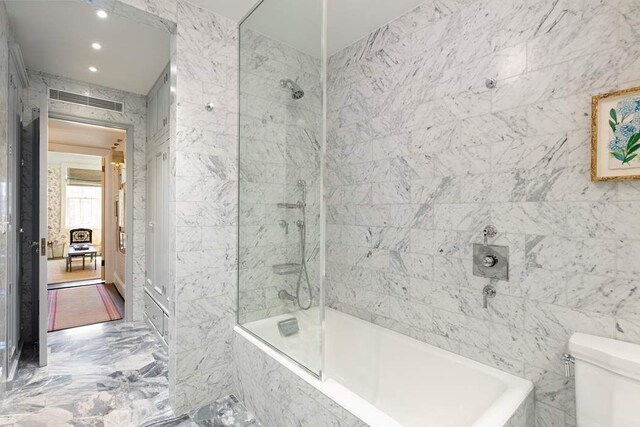 bathroom with toilet, tiled shower / bath, and tile walls