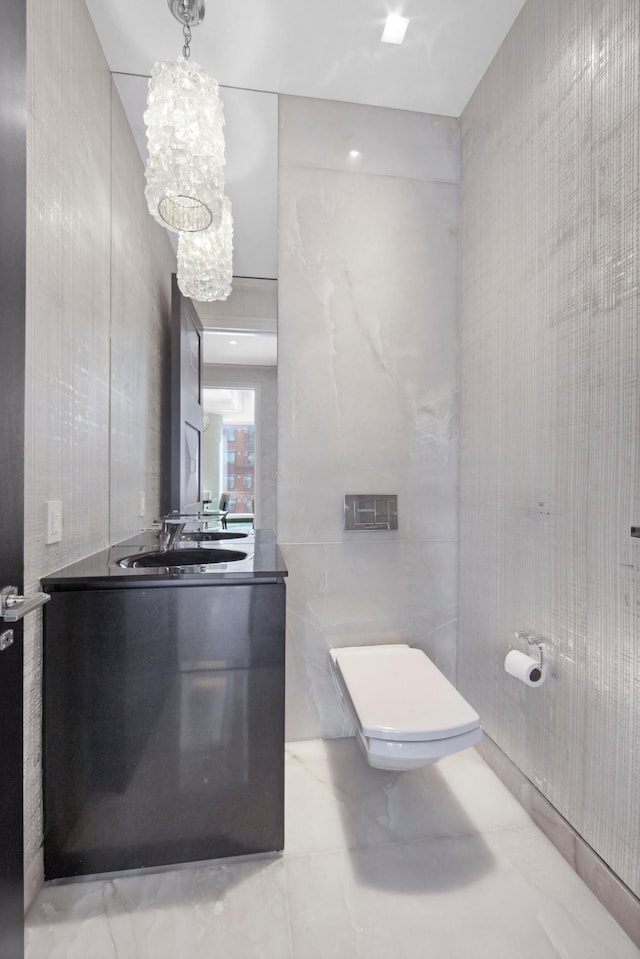 bathroom with toilet, marble finish floor, tile walls, a chandelier, and vanity