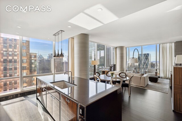 kitchen with dark wood-style flooring, a sink, a wall of windows, a city view, and a center island with sink