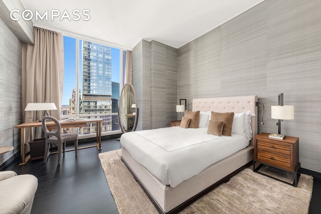 bedroom featuring wallpapered walls, floor to ceiling windows, a view of city, and wood finished floors
