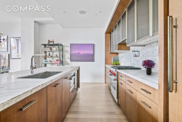 kitchen featuring sink, stainless steel stove, light hardwood / wood-style flooring, light stone countertops, and decorative backsplash