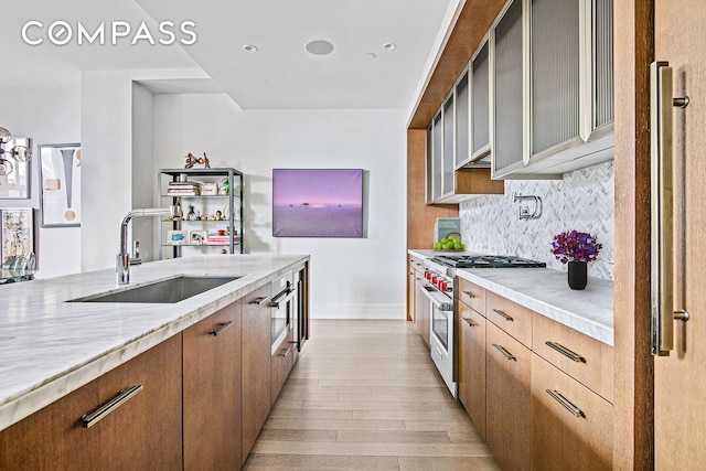 kitchen featuring light wood-style flooring, a sink, tasteful backsplash, light stone countertops, and high end range