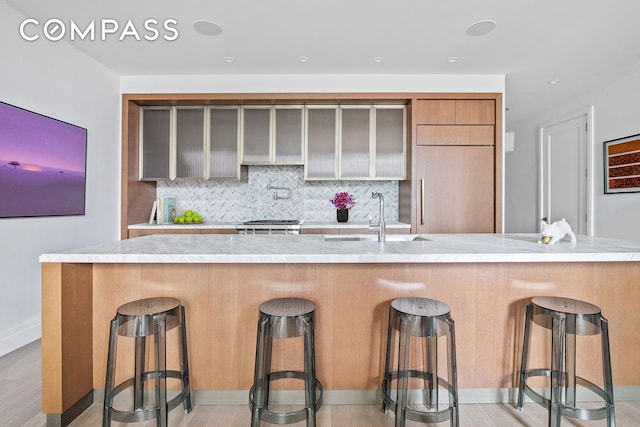 kitchen featuring decorative backsplash, light countertops, light wood-style floors, and a sink