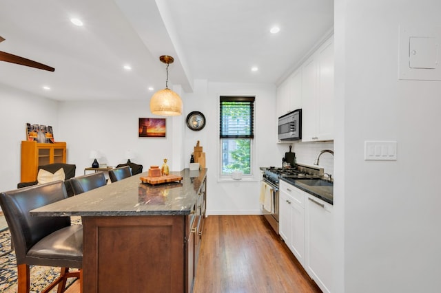 kitchen with white cabinetry, appliances with stainless steel finishes, a kitchen breakfast bar, and dark stone countertops