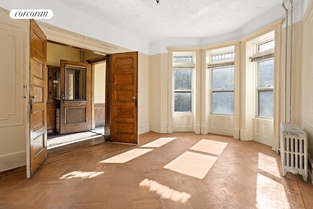 empty room with baseboards, visible vents, radiator, a textured ceiling, and a decorative wall