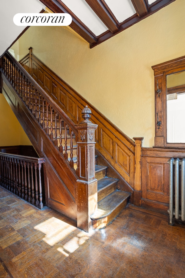 stairway with a wainscoted wall, radiator heating unit, and a decorative wall