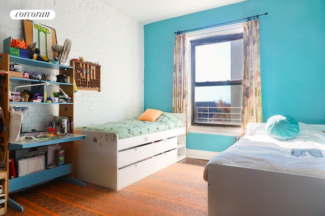 bedroom featuring brick wall, wood finished floors, and baseboards