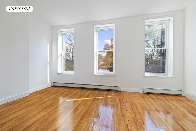 spare room featuring plenty of natural light, a baseboard heating unit, and light hardwood / wood-style flooring