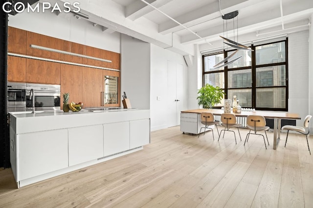 kitchen with oven, decorative light fixtures, white cabinetry, and light hardwood / wood-style flooring