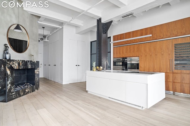 kitchen with stainless steel oven, a towering ceiling, stovetop, and light hardwood / wood-style flooring