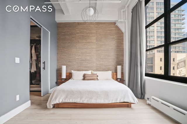 bedroom with a baseboard heating unit, a spacious closet, a closet, wood finished floors, and baseboards