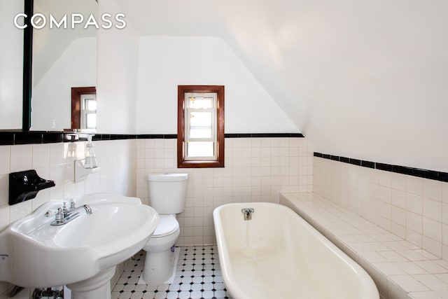 full bath featuring lofted ceiling, a freestanding tub, toilet, a wainscoted wall, and a sink