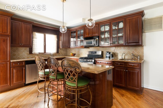 kitchen featuring stainless steel appliances, light wood finished floors, a breakfast bar area, and decorative light fixtures