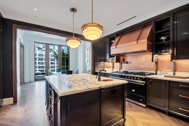 kitchen with sink, hanging light fixtures, custom range hood, an island with sink, and range with two ovens