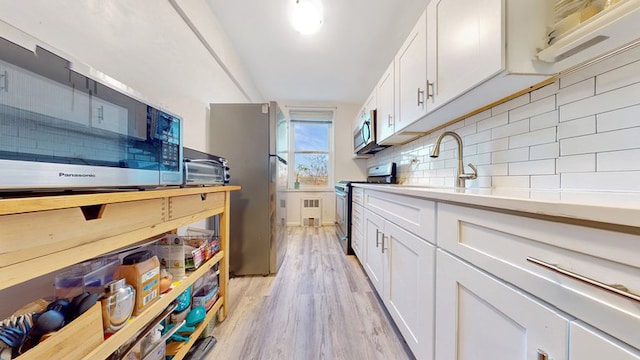 kitchen with tasteful backsplash, white cabinets, appliances with stainless steel finishes, light countertops, and a sink