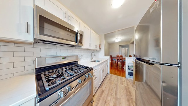 kitchen featuring white cabinetry, stainless steel appliances, sink, backsplash, and light wood-type flooring