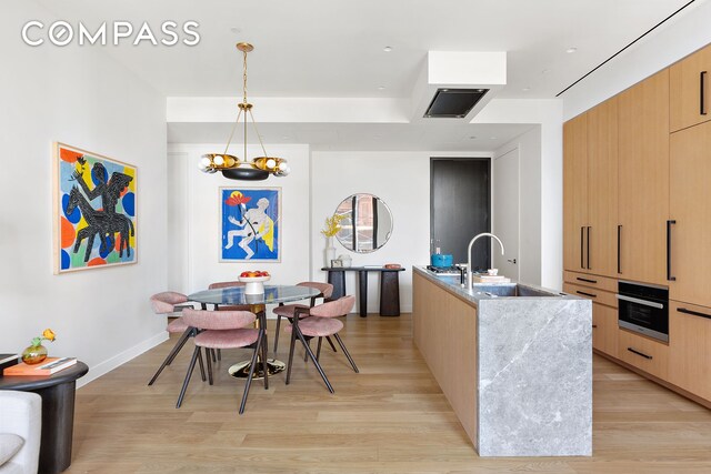 kitchen with wall oven, light brown cabinets, a sink, modern cabinets, and light wood-type flooring