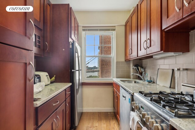 kitchen with appliances with stainless steel finishes, sink, decorative backsplash, light stone counters, and light hardwood / wood-style flooring