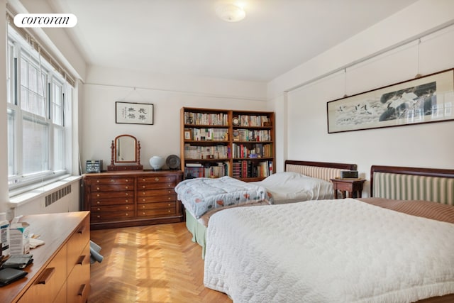 bedroom featuring multiple windows, light parquet flooring, and radiator heating unit