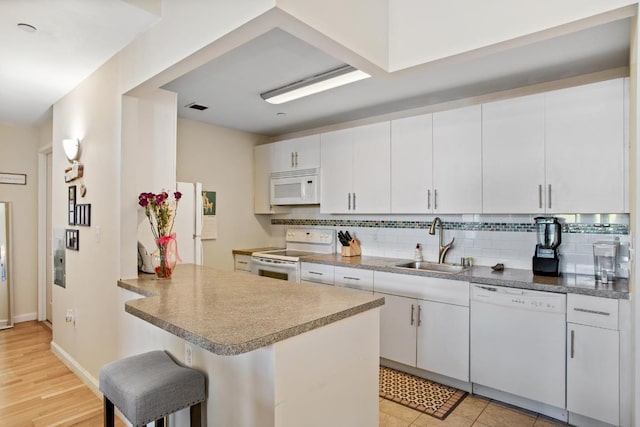 kitchen featuring sink, a kitchen breakfast bar, kitchen peninsula, white appliances, and white cabinets