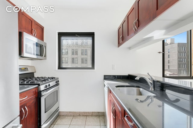 kitchen featuring reddish brown cabinets, stainless steel appliances, dark countertops, and a sink