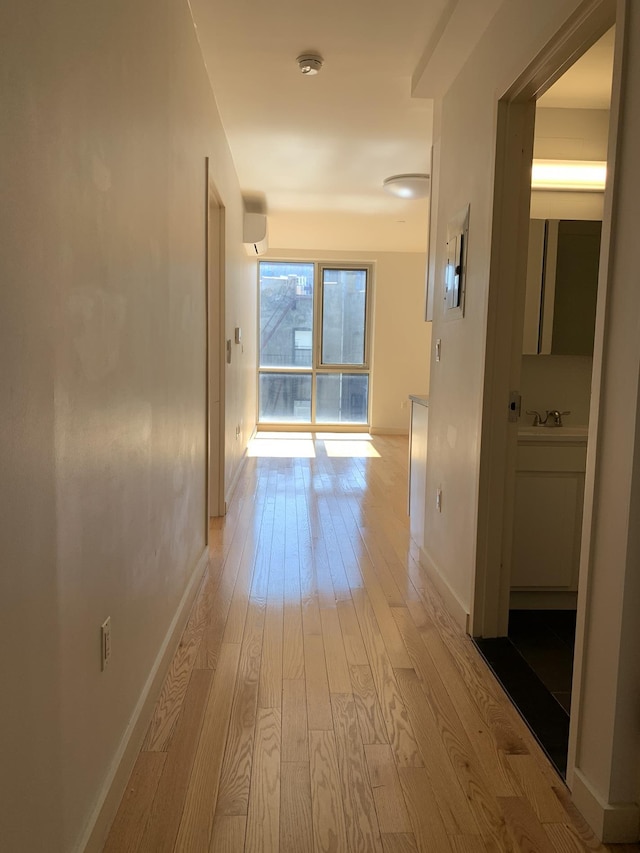 hallway featuring light wood-style flooring, baseboards, a wall unit AC, and a sink