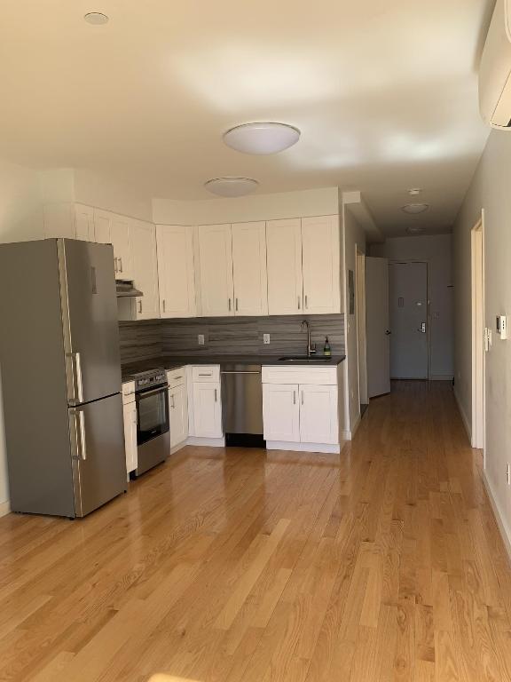 kitchen with white cabinetry, a wall unit AC, appliances with stainless steel finishes, tasteful backsplash, and sink