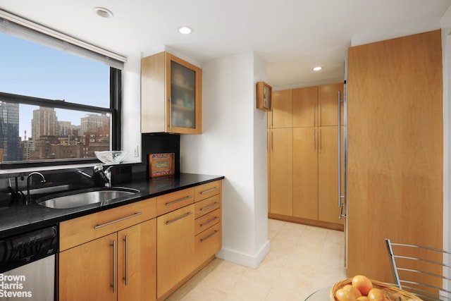 kitchen featuring light brown cabinetry, sink, stainless steel dishwasher, and dark stone countertops