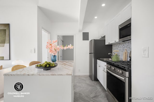 kitchen with white cabinetry, stainless steel appliances, tasteful backsplash, sink, and light stone counters