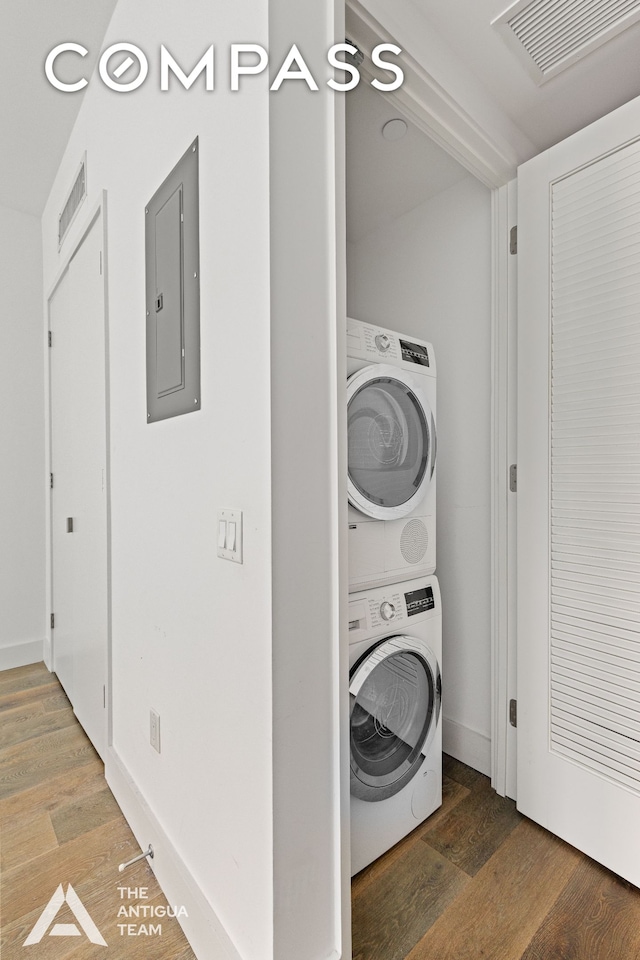 clothes washing area with laundry area, electric panel, stacked washer / dryer, and wood finished floors