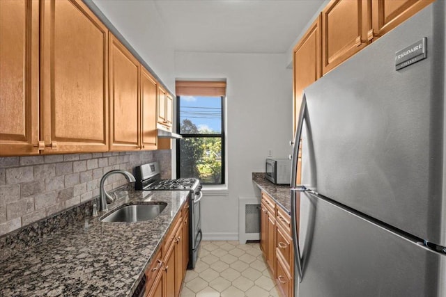 kitchen with decorative backsplash, dark stone counters, stainless steel appliances, under cabinet range hood, and a sink